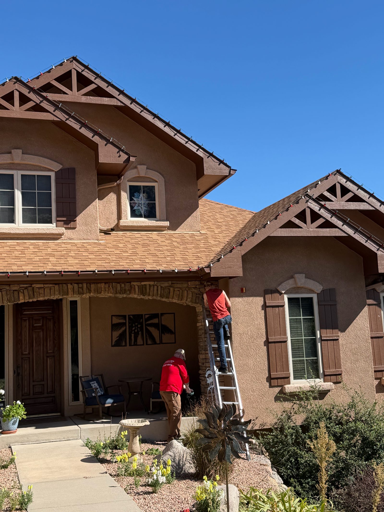 Christmas Lights Colorado Springs crew on ladder installing roofline Christmas lights by the front porch Christmas Lights Colorado Springs crew on ladder installing roofline Christmas lights by the front porch