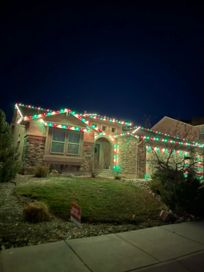 Holiday light design example - stunning Christmas lights on two-story home with multicolor LED bulbs, professional roofline lighting and landscape illumination