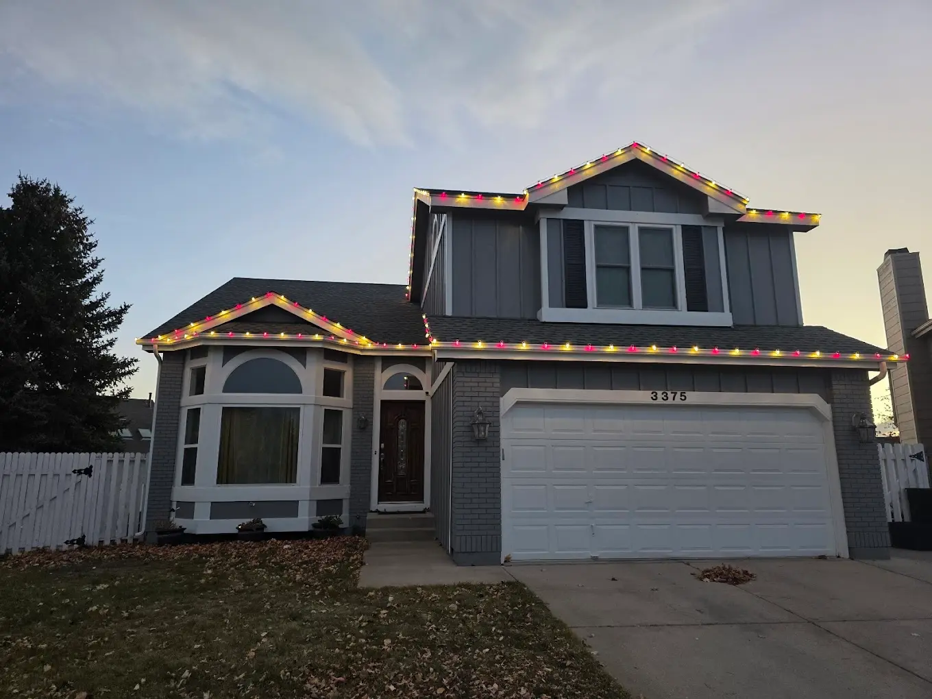Christmas light design example on two-story home - professional multicolor LED lights featuring red yellow green bulbs on roofline, residential holiday lighting services
